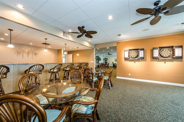 carpeted dining space with visible vents, ceiling fan, a bar, a drop ceiling, and baseboards