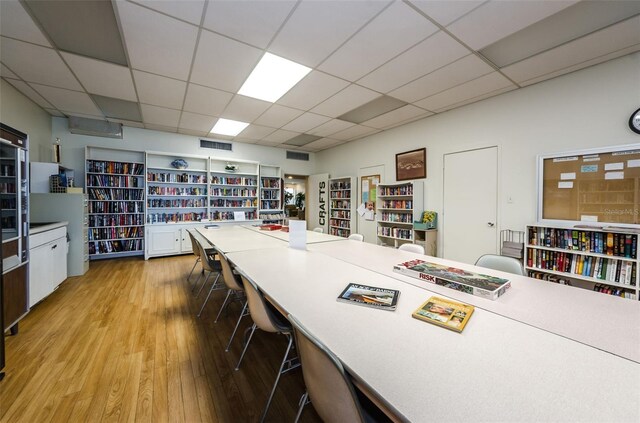 home office featuring light wood-type flooring, visible vents, a drop ceiling, and wall of books