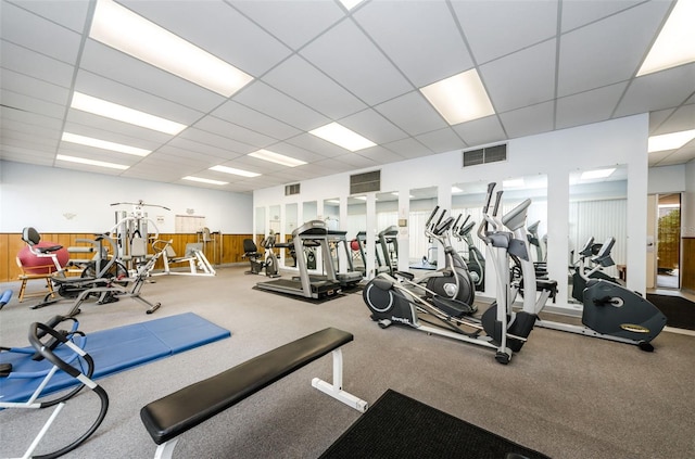 exercise room with a paneled ceiling, wainscoting, and visible vents