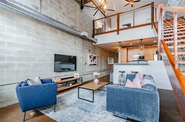 living room featuring a towering ceiling, a notable chandelier, concrete flooring, and concrete block wall