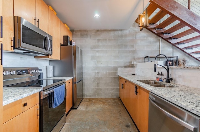 kitchen with unfinished concrete floors, appliances with stainless steel finishes, light stone counters, and a sink