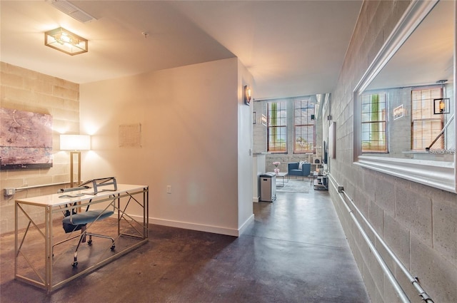 office space with concrete flooring, visible vents, concrete block wall, and baseboards