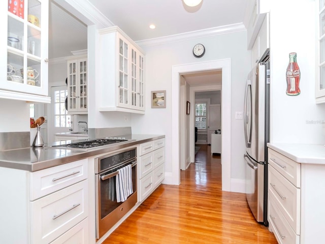 kitchen featuring stainless steel counters, appliances with stainless steel finishes, white cabinets, crown molding, and light wood finished floors