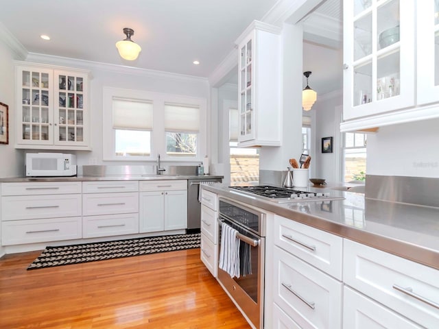 kitchen featuring stainless steel countertops, white cabinetry, stainless steel appliances, crown molding, and glass insert cabinets