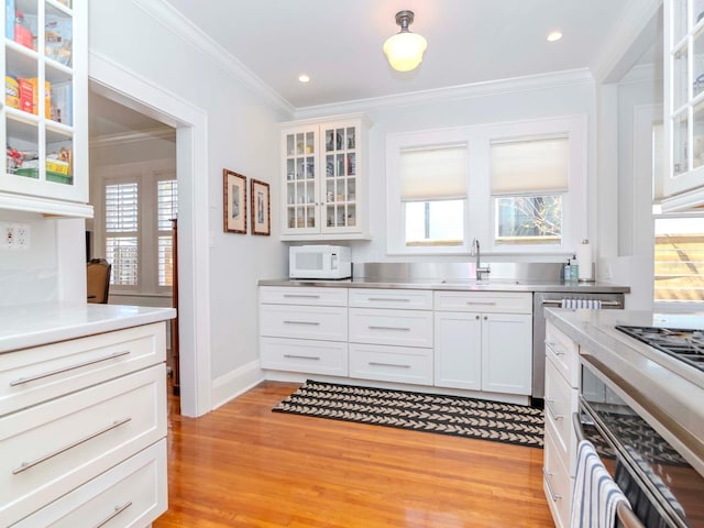 kitchen featuring white microwave, a sink, ornamental molding, white cabinets, and stainless steel counters