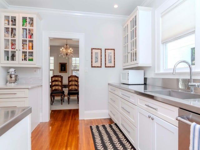 kitchen with white microwave, a sink, stainless steel countertops, dishwasher, and crown molding