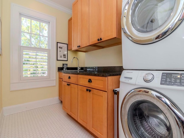 washroom featuring baseboards, ornamental molding, stacked washer and clothes dryer, cabinet space, and a sink