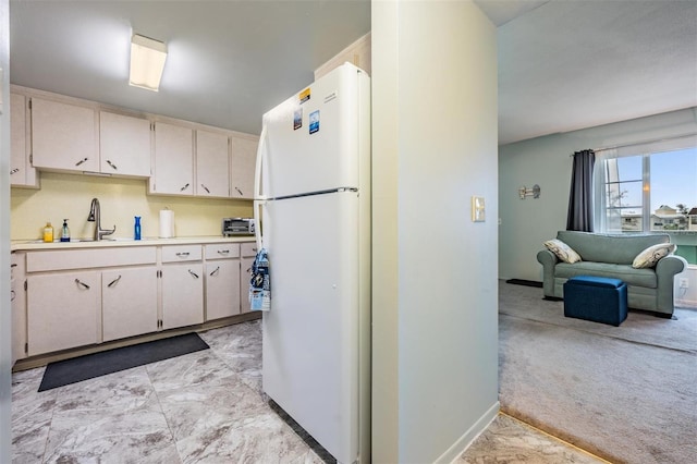 kitchen featuring light carpet, a sink, baseboards, light countertops, and freestanding refrigerator