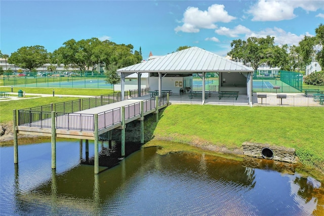 view of dock featuring a water view, fence, and a lawn