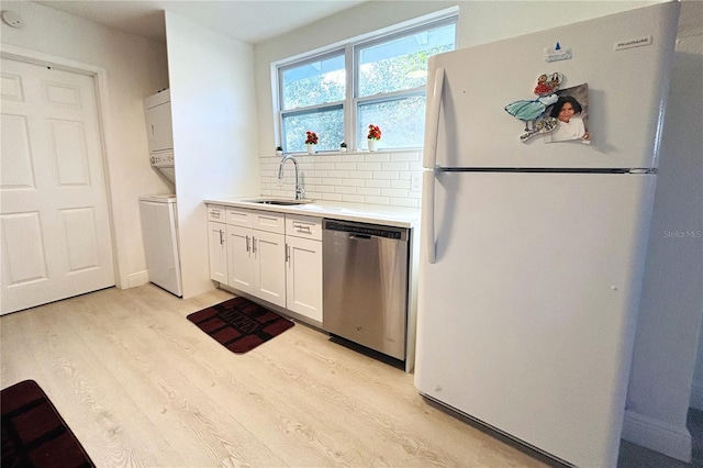 kitchen with light wood-style flooring, stainless steel dishwasher, freestanding refrigerator, stacked washer / dryer, and a sink