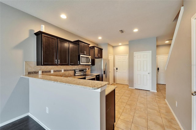 kitchen with light stone counters, visible vents, backsplash, appliances with stainless steel finishes, and dark brown cabinetry