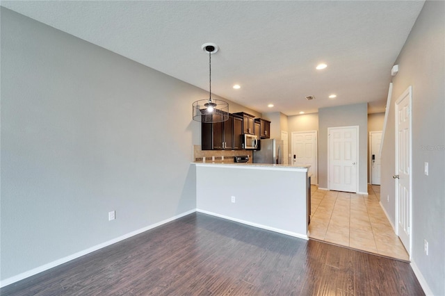 kitchen with wood finished floors, dark brown cabinets, appliances with stainless steel finishes, light countertops, and decorative backsplash