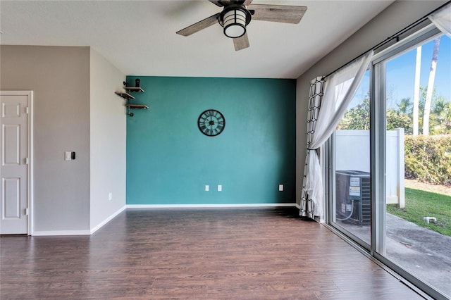 empty room featuring ceiling fan, an accent wall, wood finished floors, and baseboards