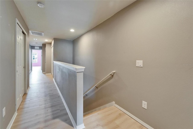 corridor with visible vents, light wood-type flooring, and an upstairs landing