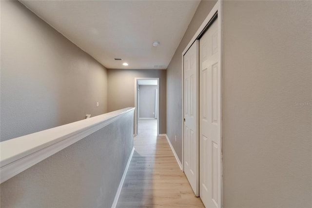 hall with light wood-style floors, visible vents, baseboards, and an upstairs landing