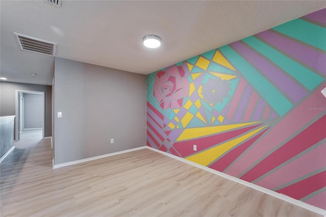 empty room featuring an accent wall, wood finished floors, visible vents, and baseboards