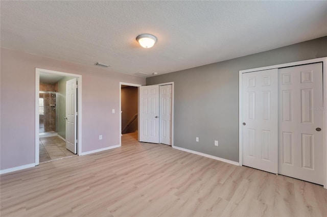 unfurnished bedroom featuring a textured ceiling, light wood finished floors, visible vents, and multiple closets