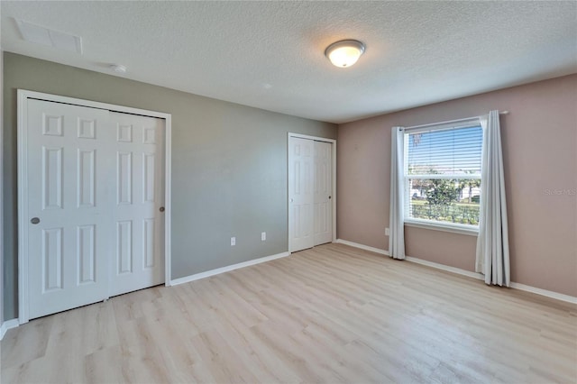 unfurnished bedroom with a textured ceiling, light wood-style flooring, baseboards, and two closets