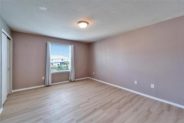 empty room with light wood-style floors, baseboards, and a textured ceiling