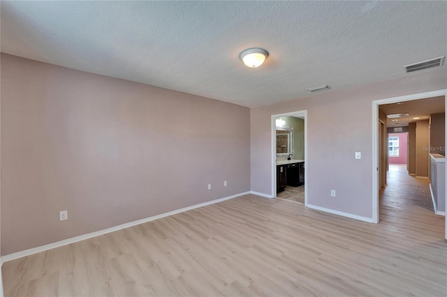 interior space with light wood-style floors, visible vents, a textured ceiling, and baseboards