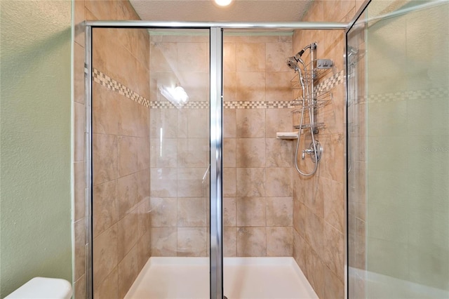 bathroom featuring toilet, a stall shower, and a textured wall