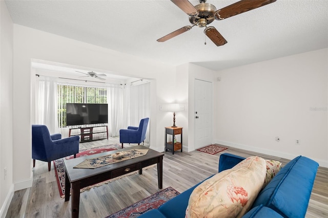 living area with a textured ceiling, light wood-type flooring, a ceiling fan, and baseboards