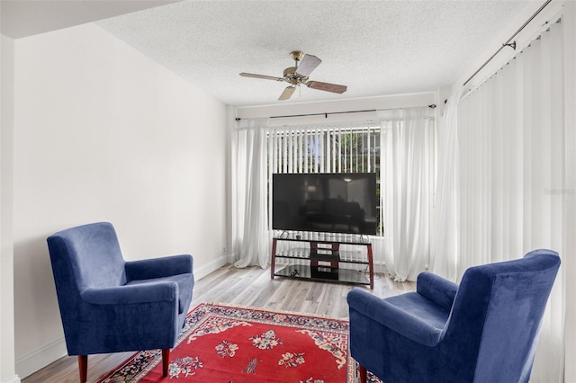 living room featuring a ceiling fan, a textured ceiling, baseboards, and wood finished floors