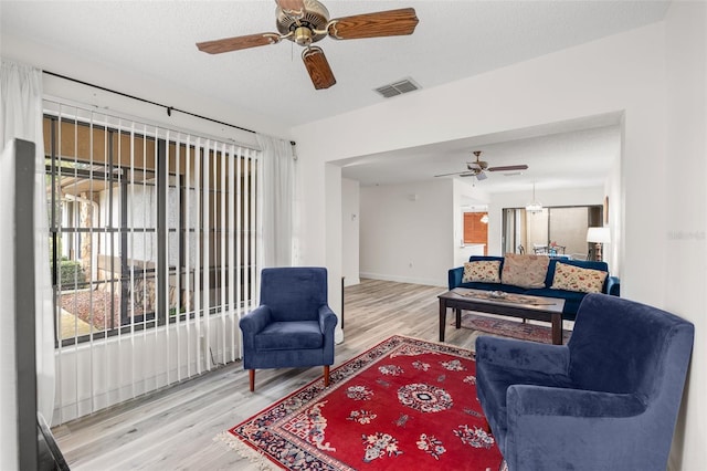 living area with a textured ceiling, wood finished floors, a ceiling fan, visible vents, and baseboards