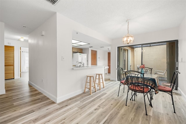 dining room featuring light wood-type flooring, visible vents, and a textured ceiling