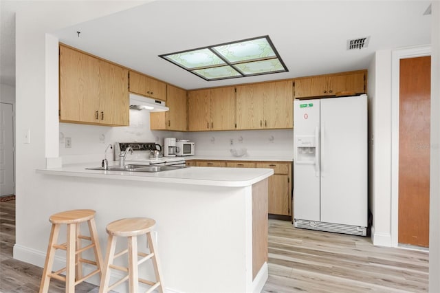 kitchen featuring light countertops, white refrigerator with ice dispenser, a peninsula, and under cabinet range hood