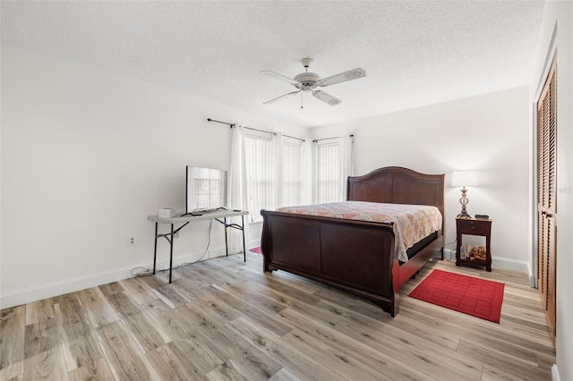 bedroom featuring light wood finished floors, a ceiling fan, baseboards, and a textured ceiling