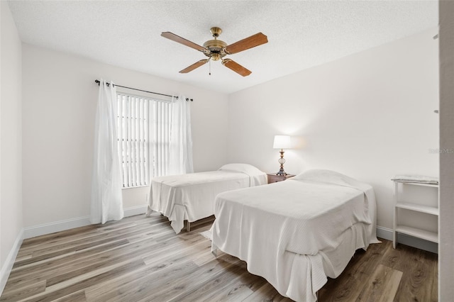 bedroom featuring light wood-type flooring, a ceiling fan, baseboards, and a textured ceiling