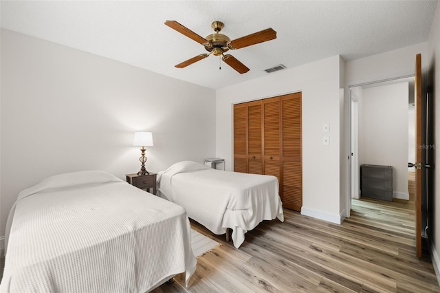 bedroom with baseboards, visible vents, a ceiling fan, light wood-type flooring, and a closet