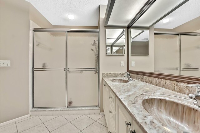 full bathroom featuring a textured ceiling, tile patterned flooring, a sink, and a shower stall