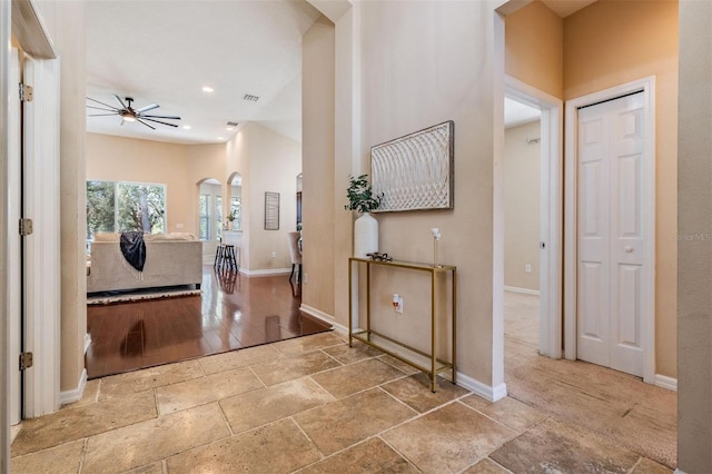 corridor featuring baseboards, visible vents, arched walkways, and stone tile flooring