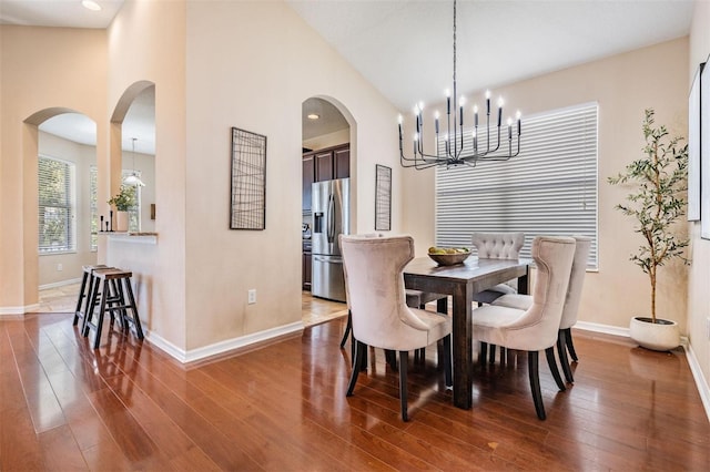 dining space featuring arched walkways, high vaulted ceiling, dark wood-style flooring, and baseboards