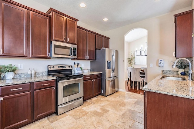 kitchen with arched walkways, light stone counters, stainless steel appliances, a sink, and recessed lighting