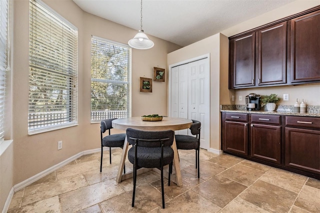 dining space featuring a healthy amount of sunlight, stone tile floors, a textured ceiling, and baseboards