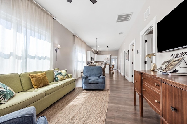 living area featuring baseboards, visible vents, dark wood-style flooring, and ceiling fan with notable chandelier