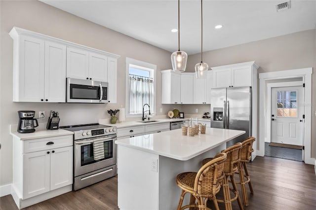 kitchen featuring a center island, pendant lighting, stainless steel appliances, light countertops, and white cabinetry