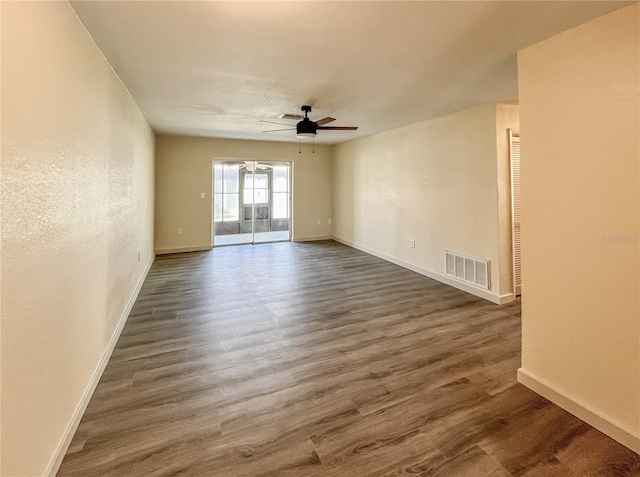 empty room with a ceiling fan, dark wood-style flooring, visible vents, and baseboards