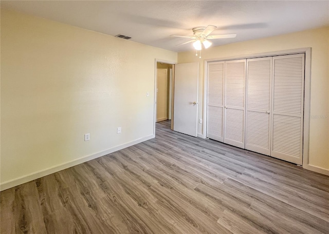 unfurnished bedroom with baseboards, visible vents, ceiling fan, wood finished floors, and a closet