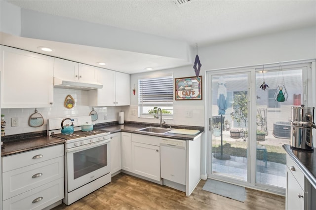 kitchen featuring white appliances, dark countertops, under cabinet range hood, and a sink