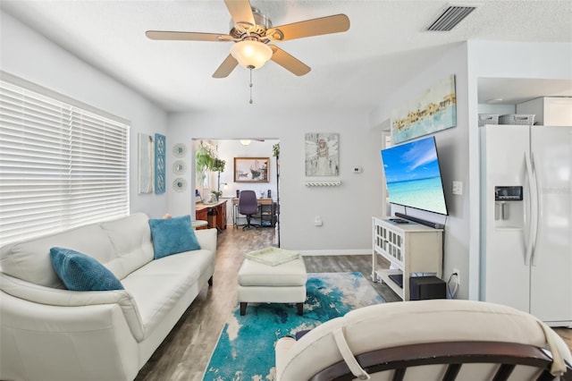 living area with visible vents, a ceiling fan, a textured ceiling, wood finished floors, and baseboards