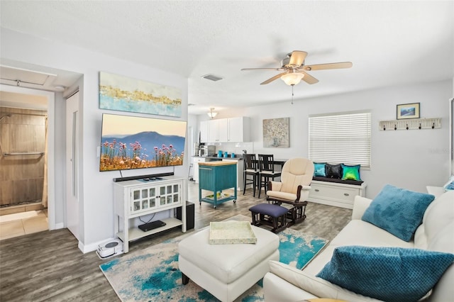 living area with visible vents, a ceiling fan, a textured ceiling, wood finished floors, and baseboards