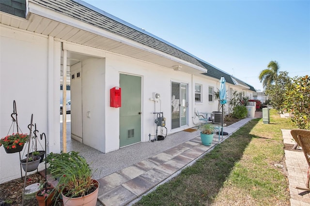 exterior space featuring central AC, stucco siding, a shingled roof, a patio area, and a lawn