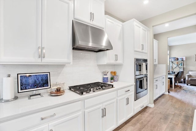 kitchen with under cabinet range hood, white cabinets, light countertops, appliances with stainless steel finishes, and light wood finished floors