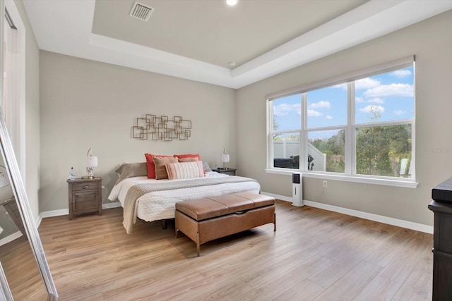 bedroom featuring visible vents, a tray ceiling, and light wood-style flooring