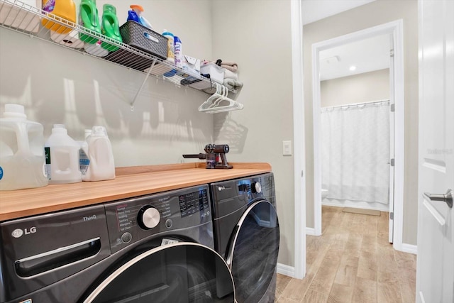 clothes washing area with baseboards, laundry area, washing machine and dryer, and light wood-style floors