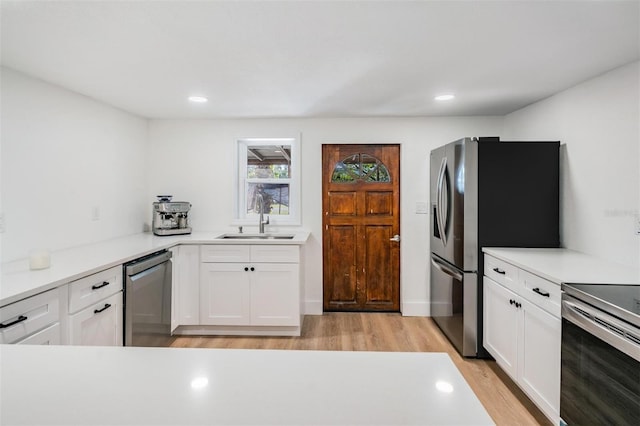 kitchen with a sink, white cabinetry, light countertops, appliances with stainless steel finishes, and light wood finished floors